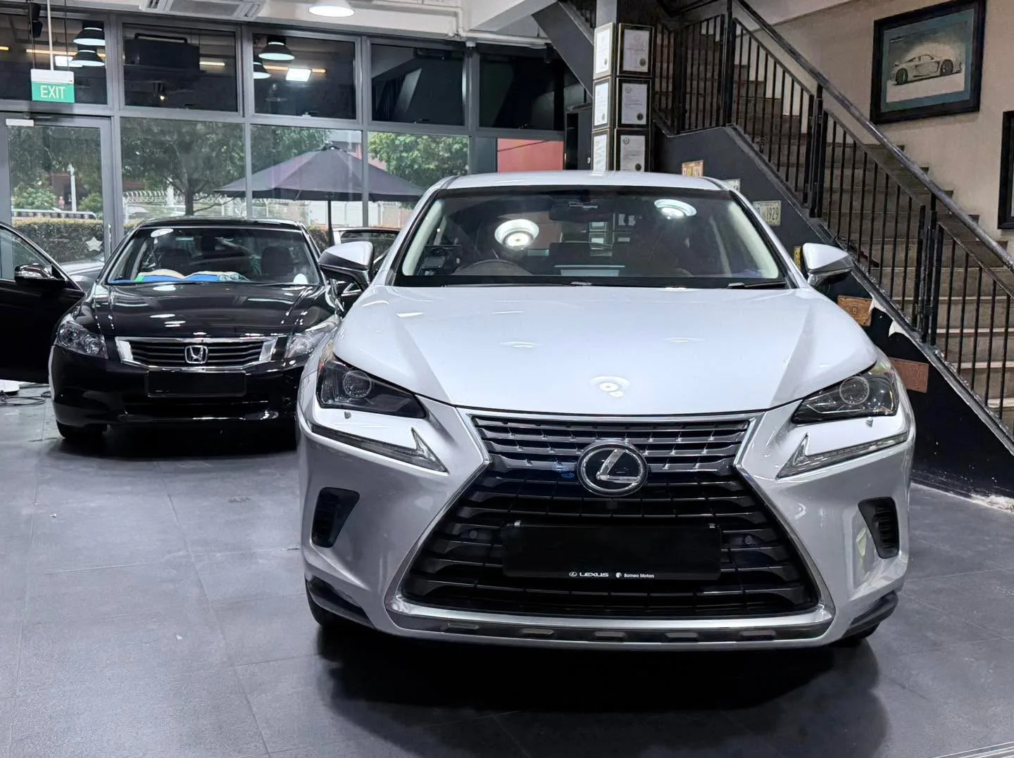 A white Lexus NX300 and black Honda Accord parked indoors beside large windows.