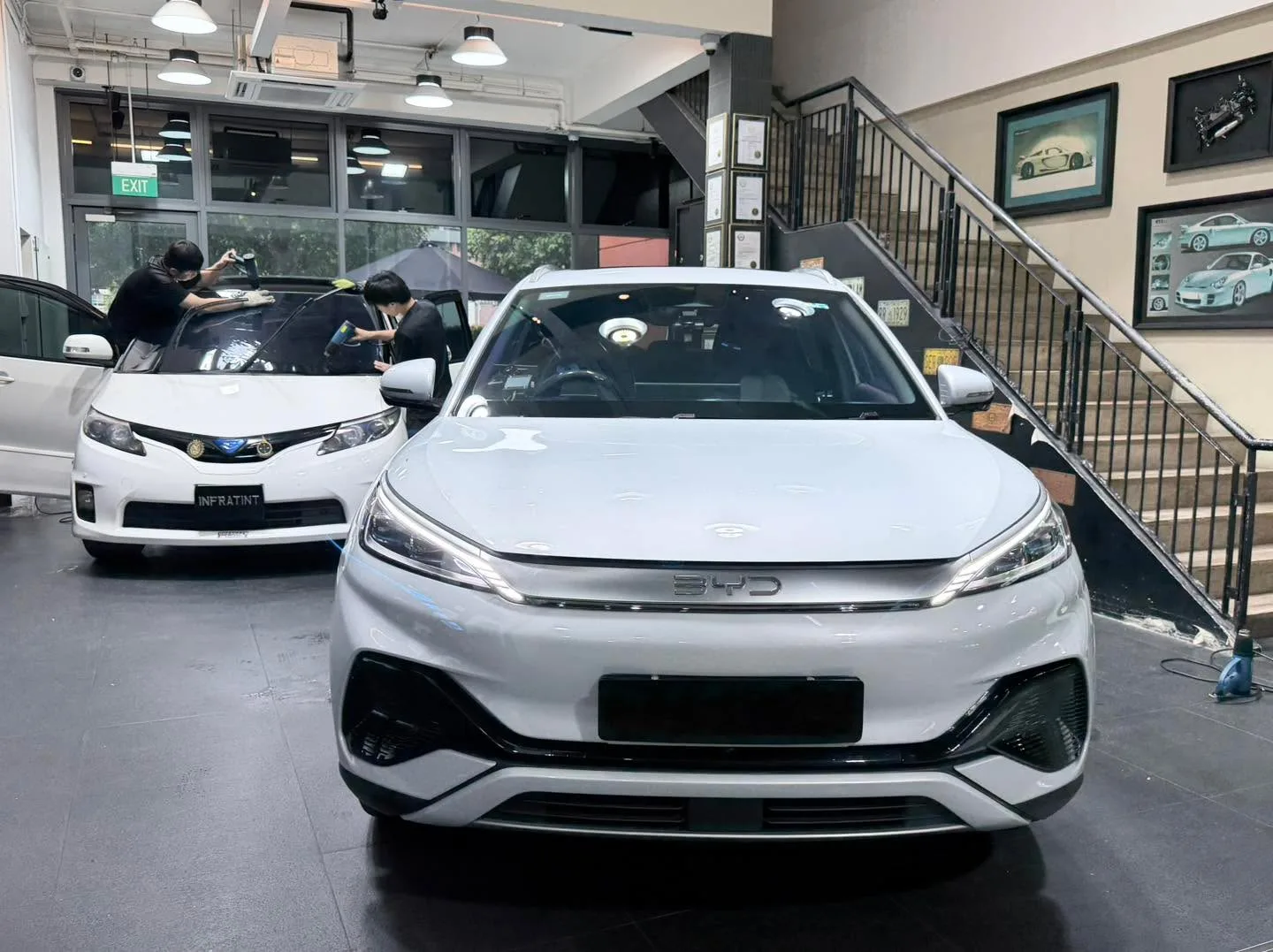 A white BYD Atto 3 and white Honda Accord inside the workshop with staff working.