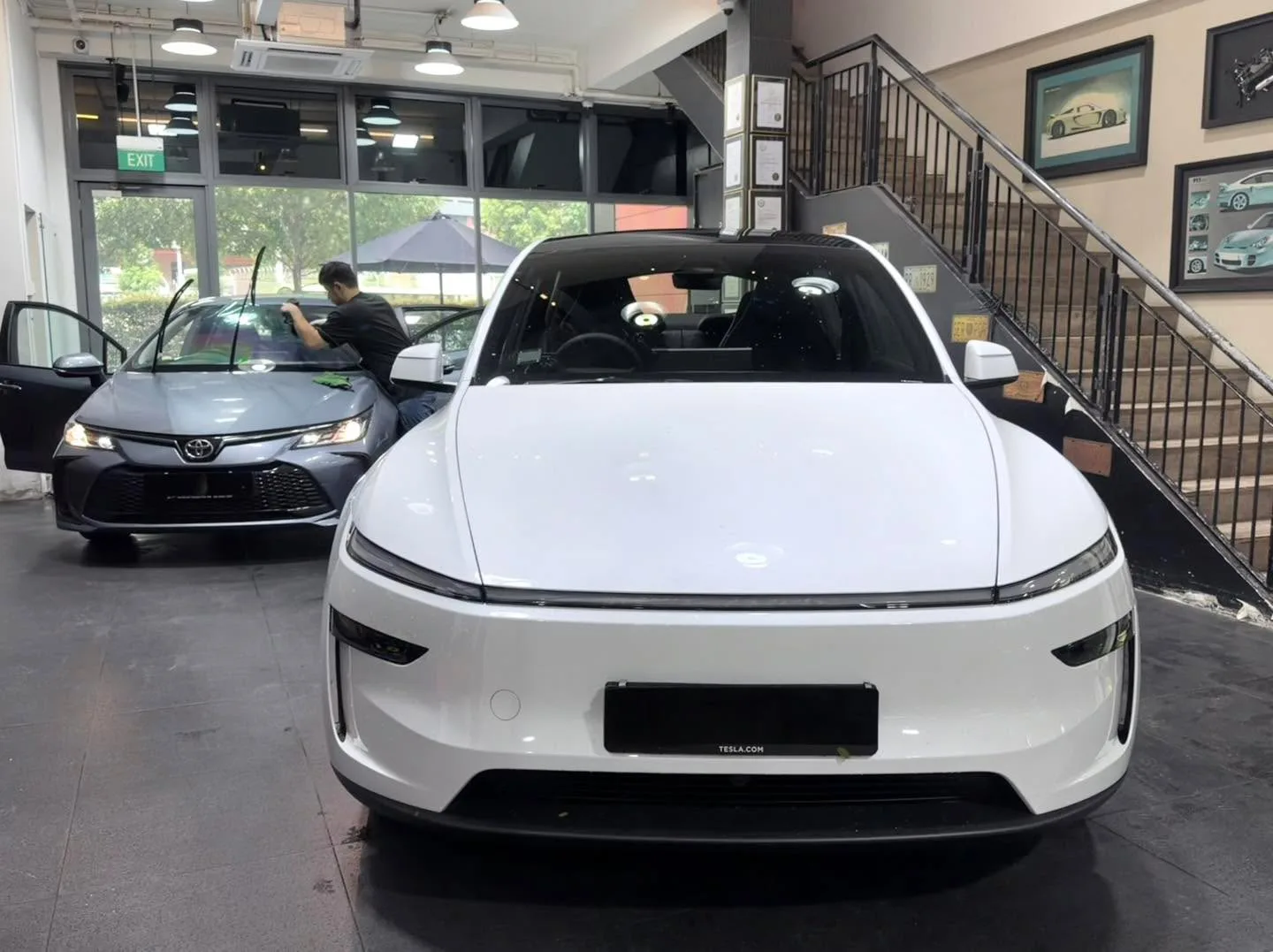A white electric sedan with distinctive front end and Tesla badging visible, positioned indoors.