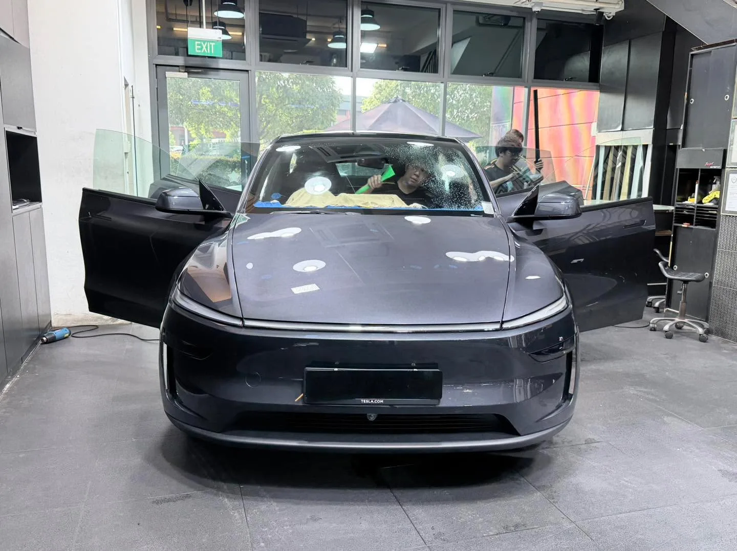 A dark grey electric sedan with characteristic front design and open doors indoors.