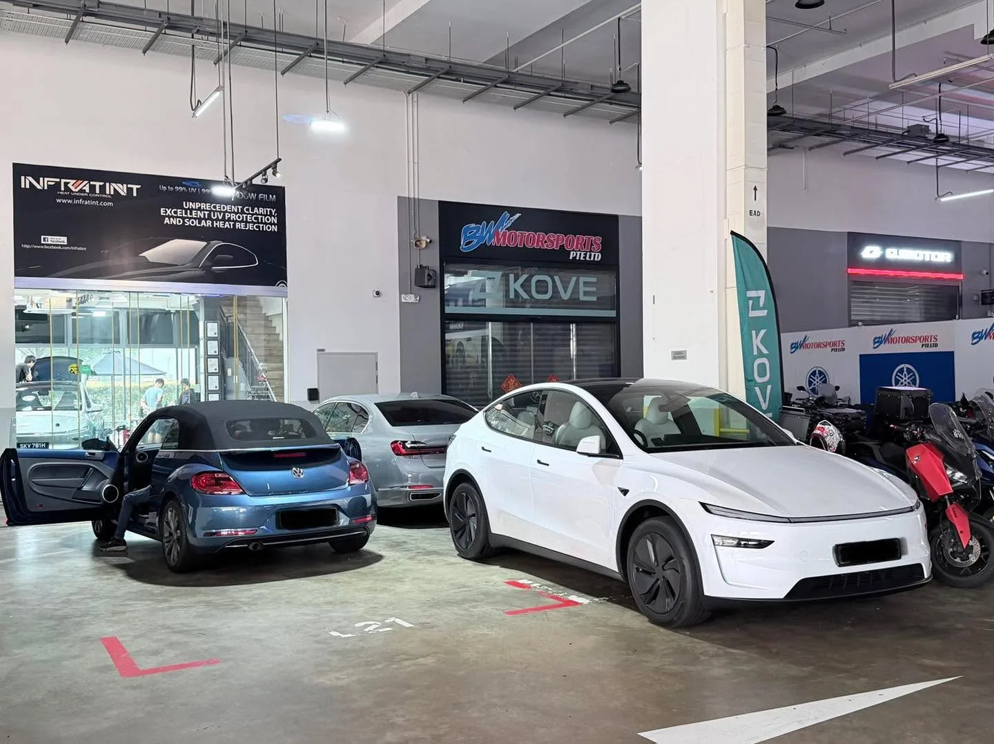 A blue SUV and white sedan parked indoors under workshop lighting.