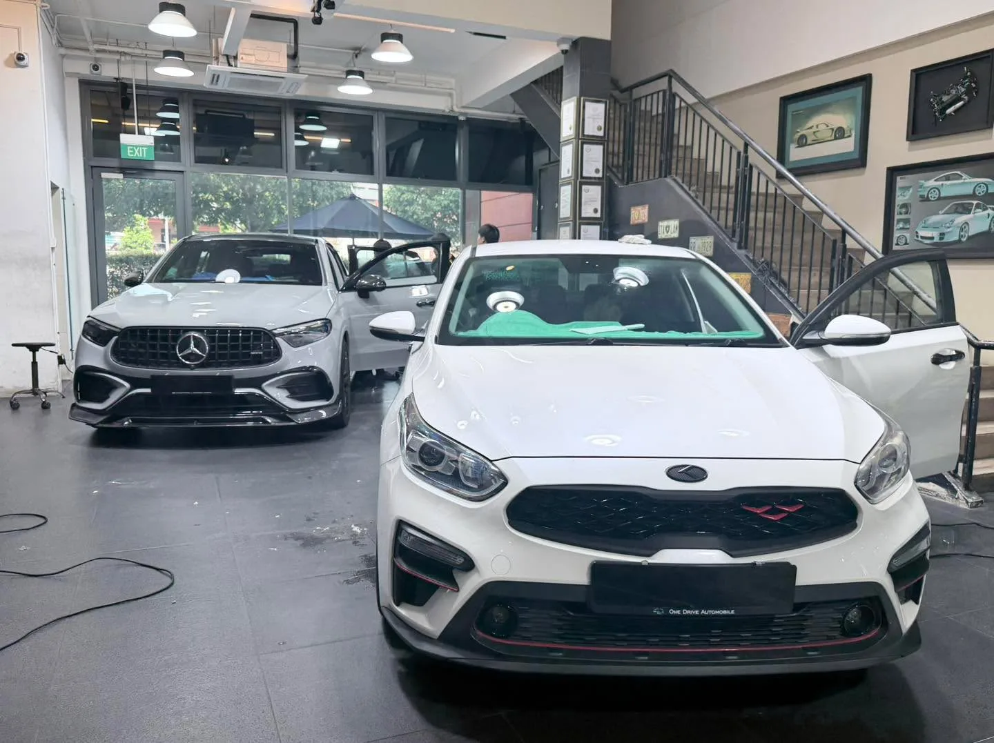 A white compact sedan with dark mesh grille in a workshop bay.