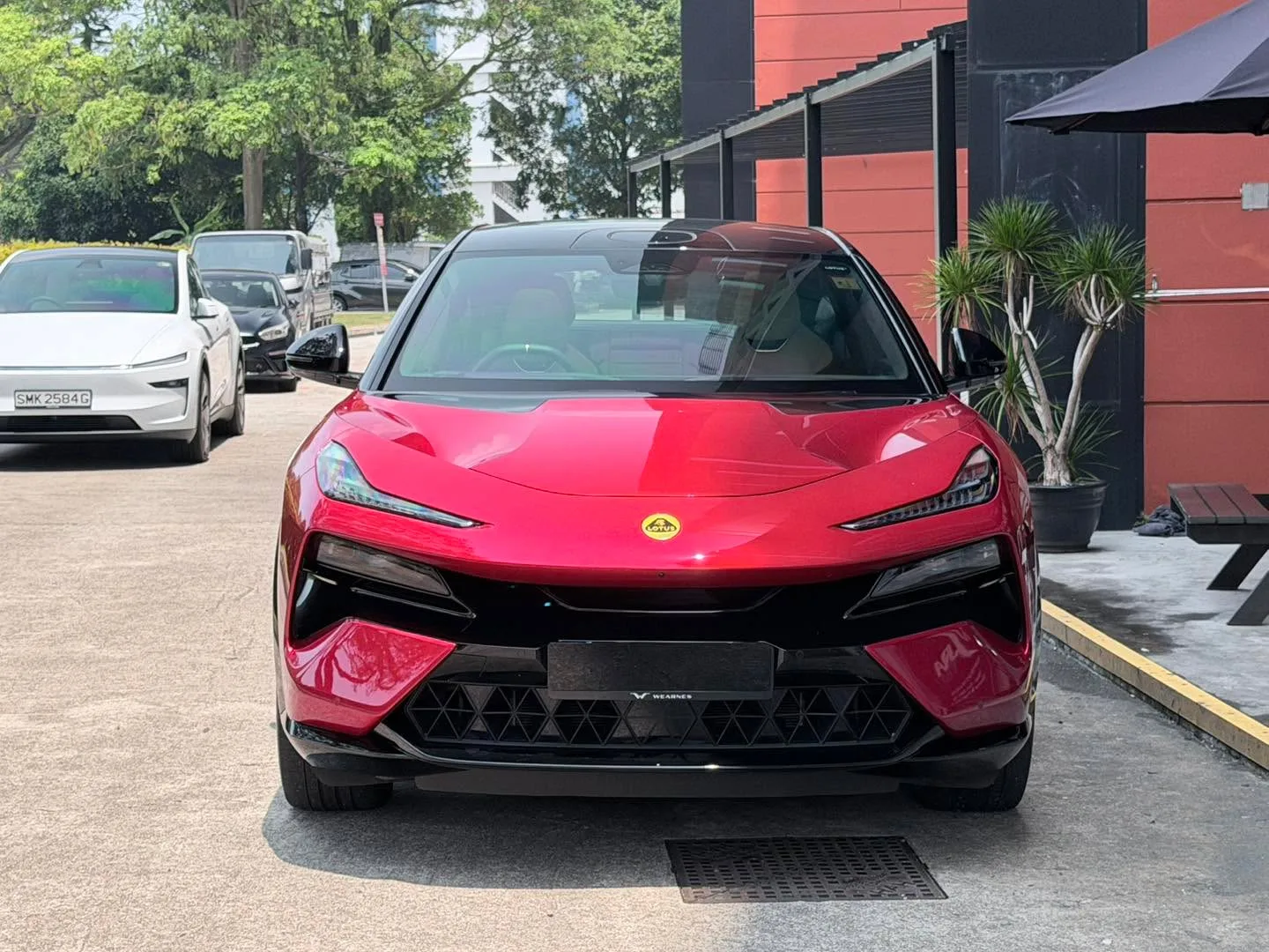 A red Lotus Eletre parked at the workshop entrance with other vehicles in the background.