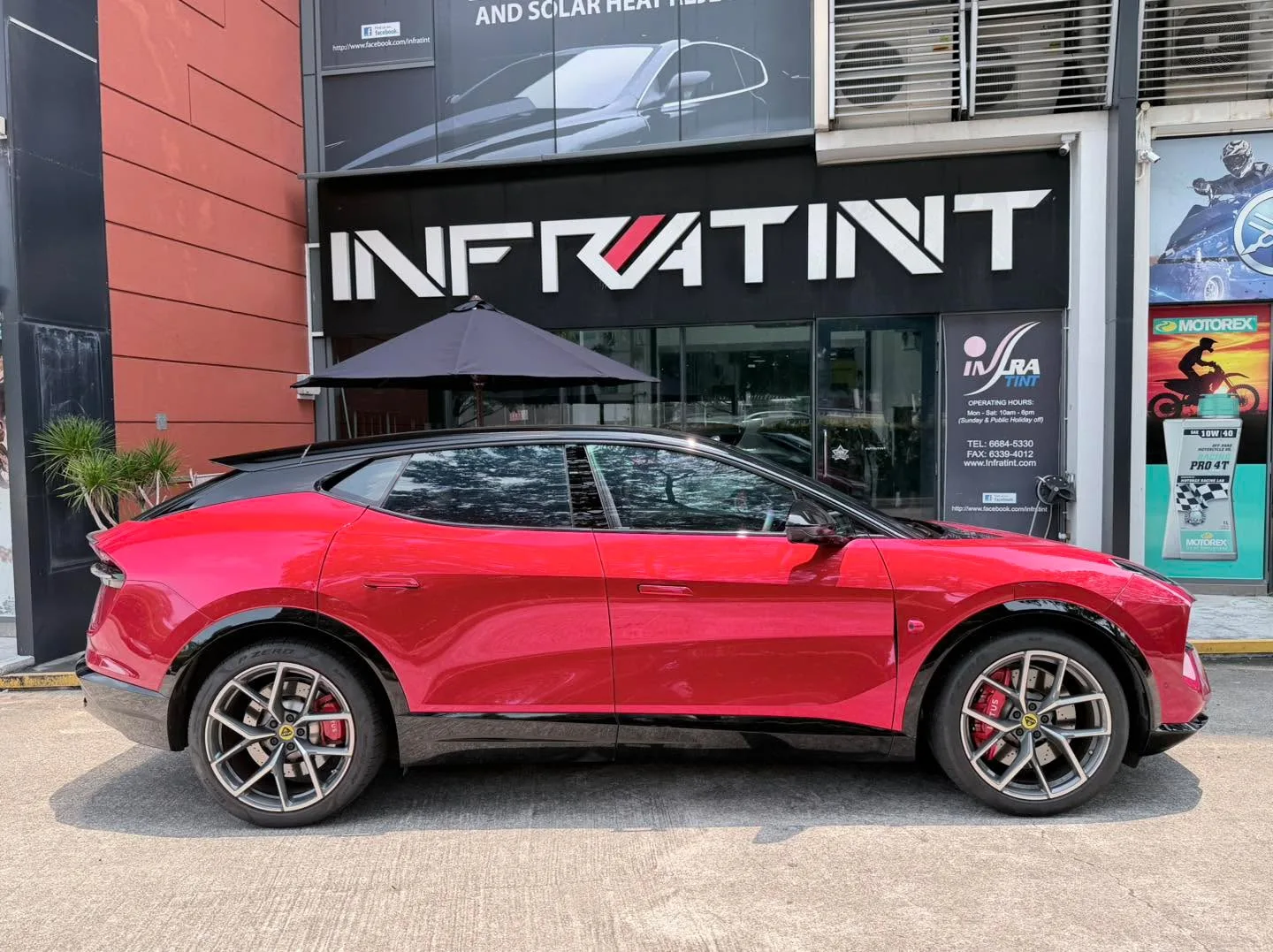 A red Lotus Eletre positioned outside the workshop storefront showing its side profile.
