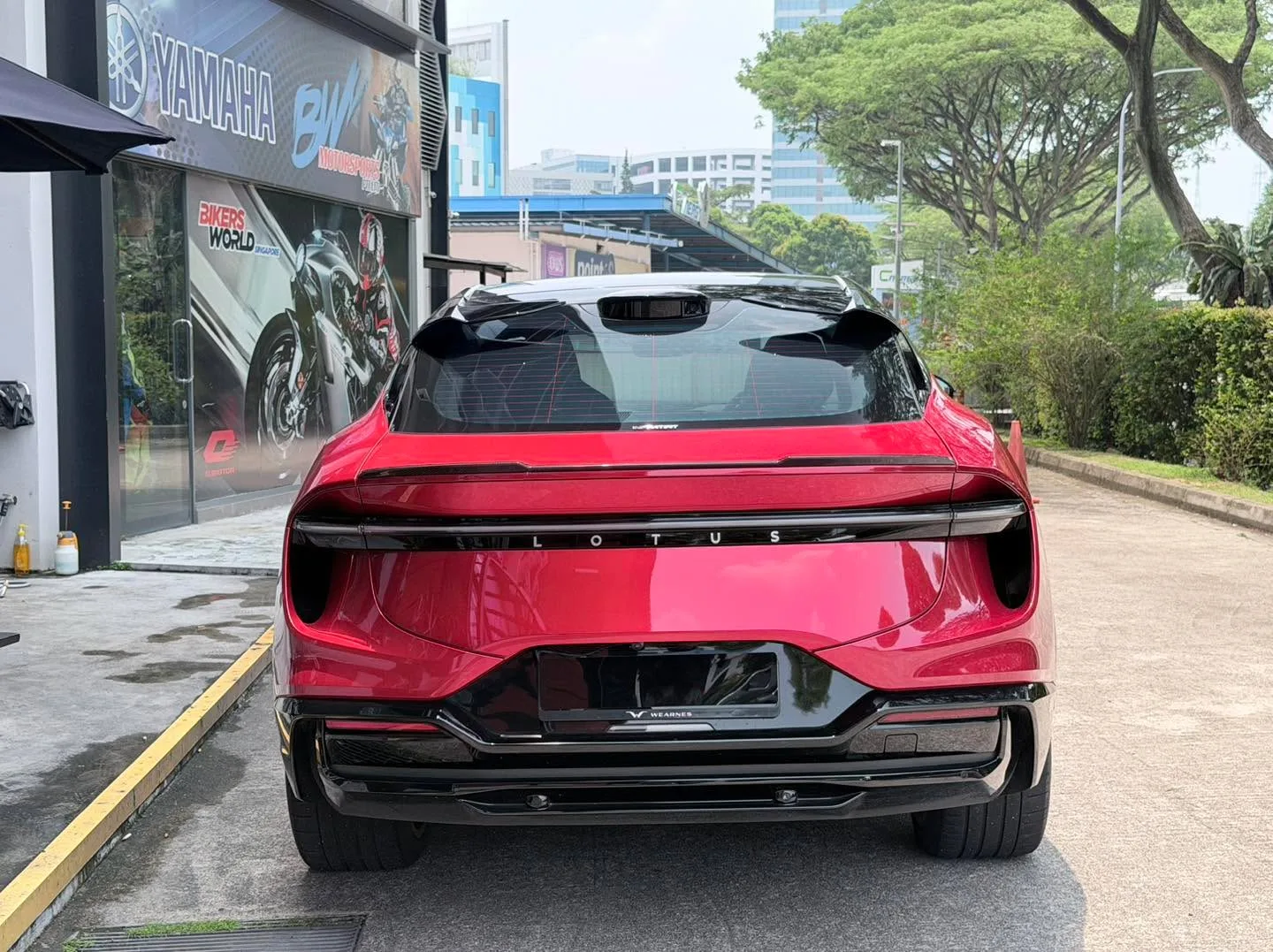 The rear view of a red Lotus Eletre with black trim parked on a street with trees and buildings visible.