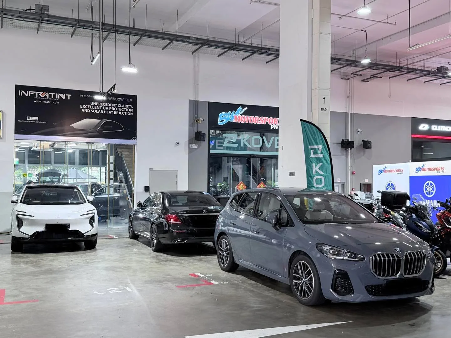 A white electric car, a black sedan, a grey BMW, and a red minivan in a showroom.