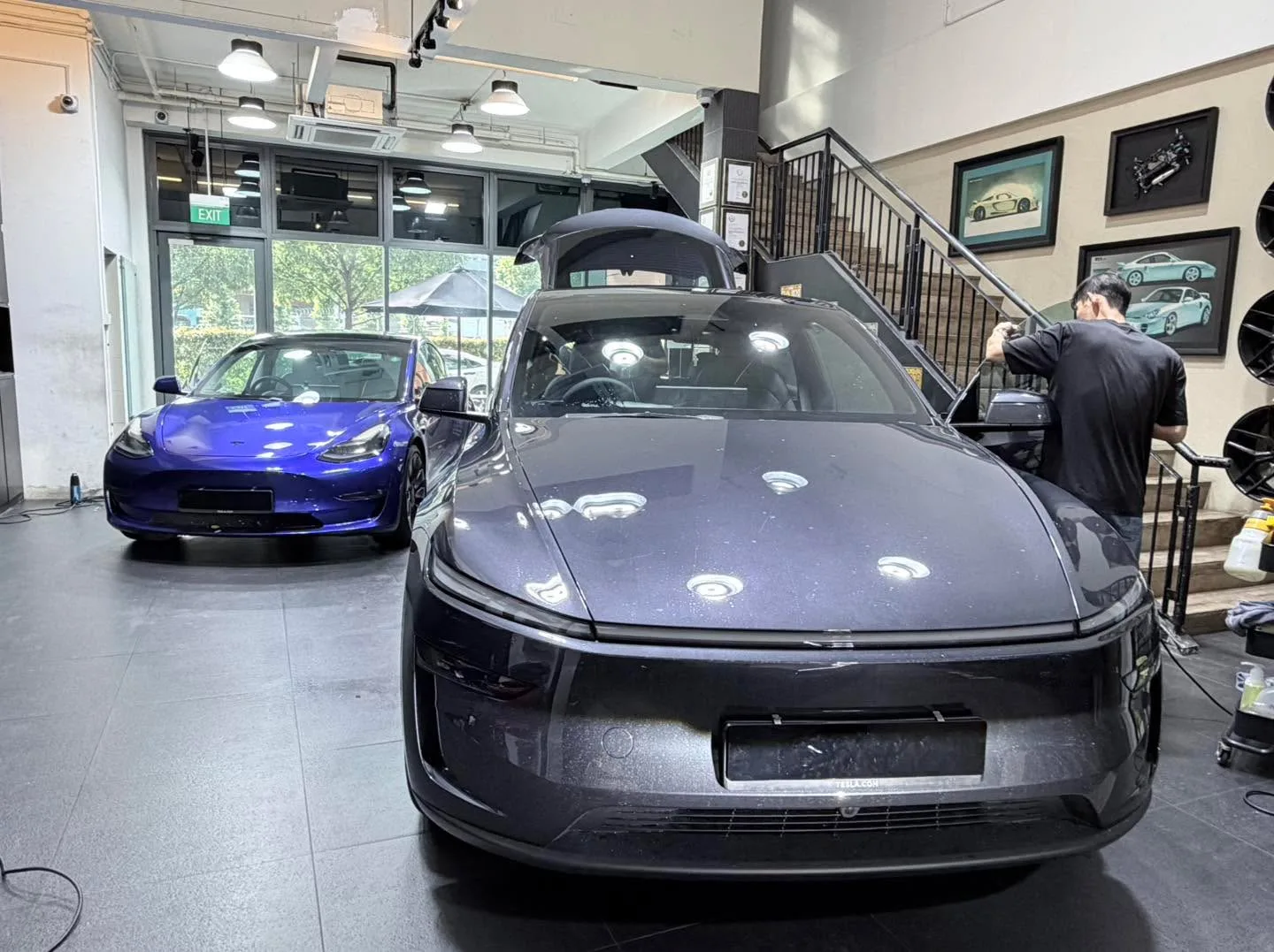 A blue Tesla and a dark grey electric sedan in the workshop with staff working nearby.