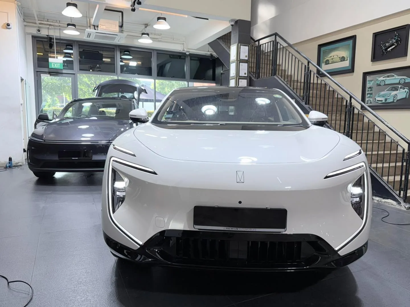 A white electric sedan with gull-wing doors and a black vehicle in the workshop.
