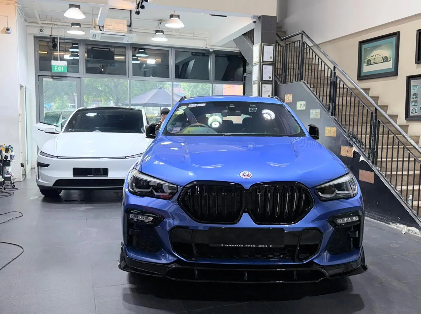 A blue BMW X6 40i facing the camera with a white Tesla Model Y behind it.