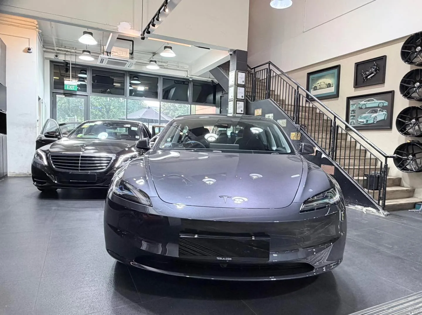 A dark Mercedes-Benz sedan and a dark Tesla sedan parked in the workshop.
