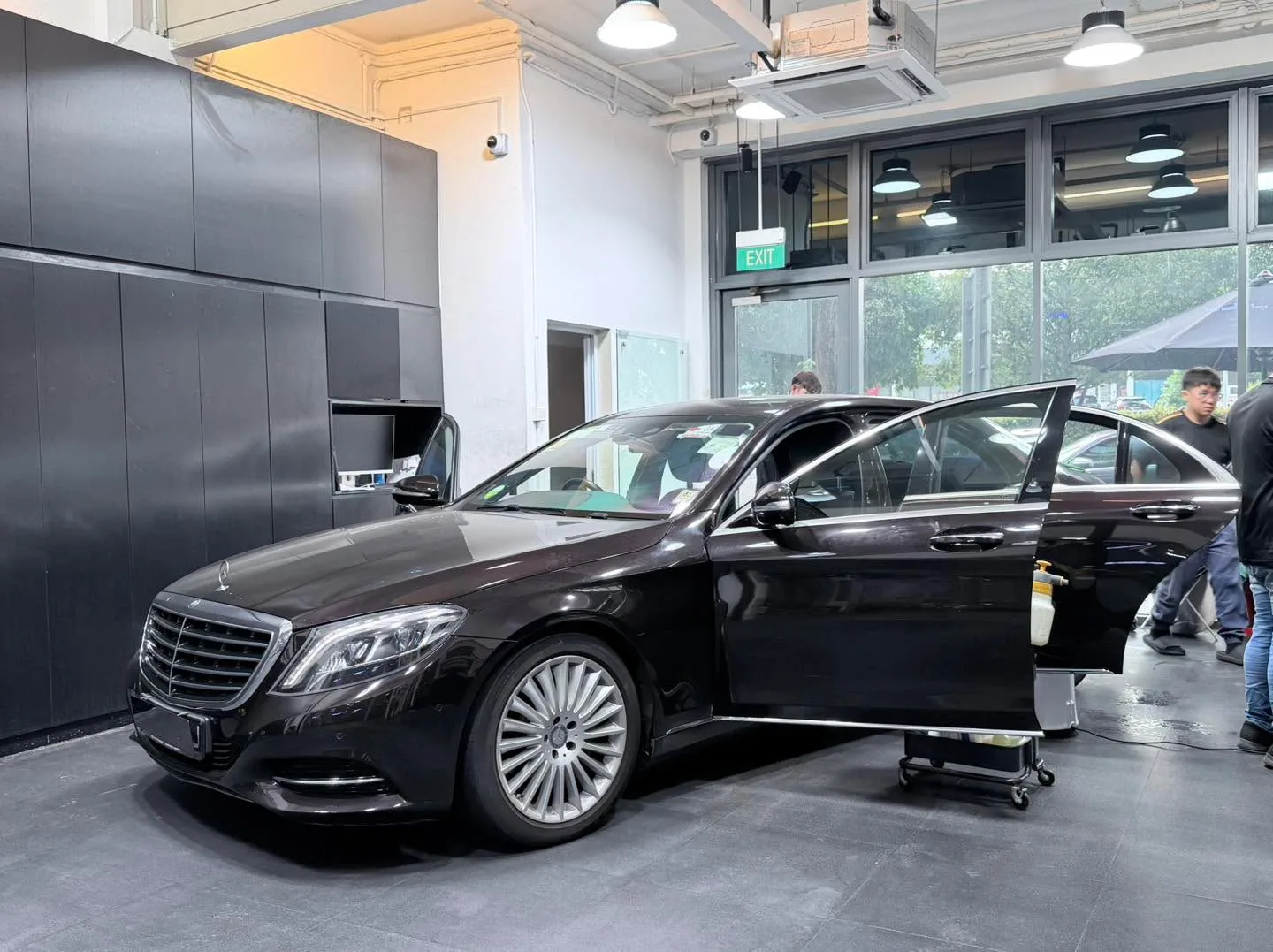 A black Mercedes-Benz sedan with doors open in the workshop from another angle.