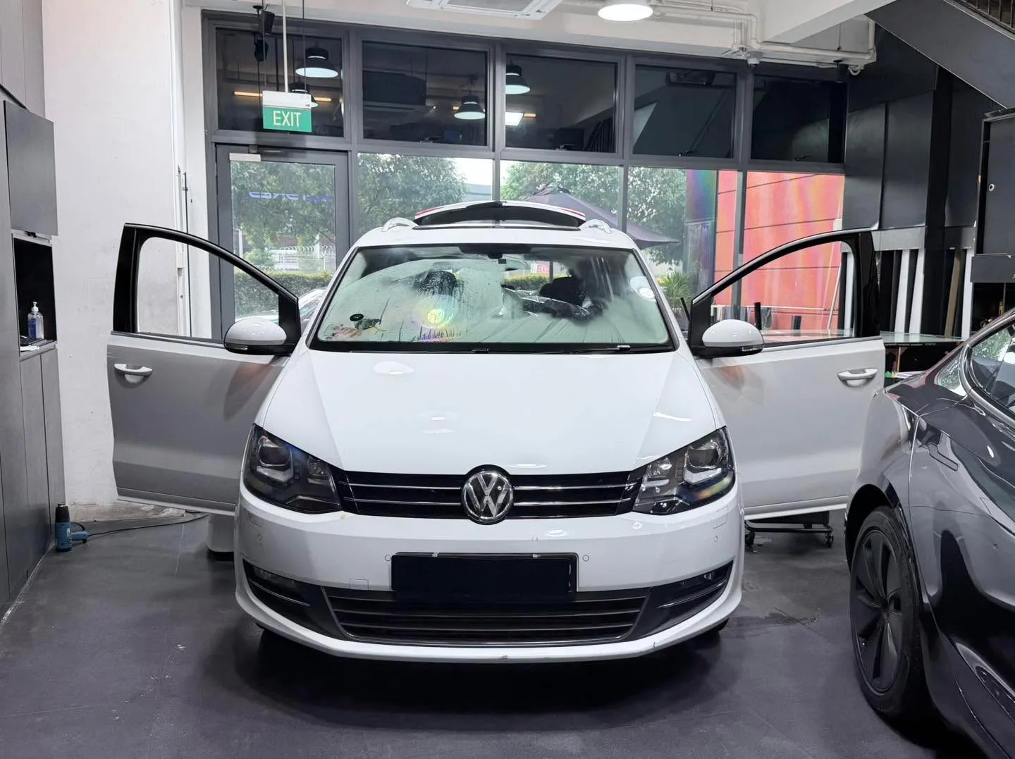 A white Porsche SUV parked in the workshop with another vehicle behind it.