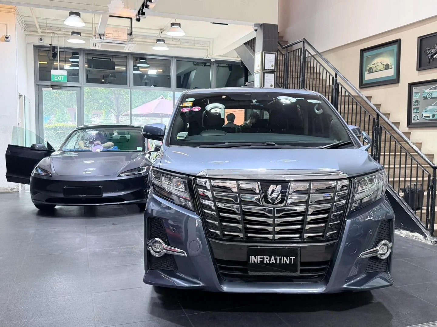 A dark Toyota Alphard and a dark Tesla sedan in the workshop.