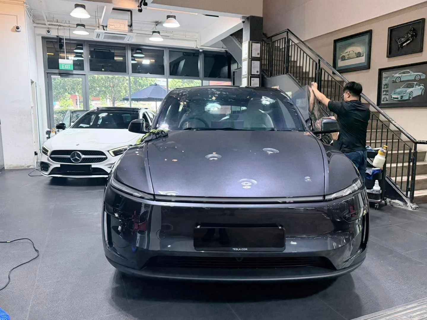 A dark Tesla sedan with doors open and a technician applying window film.