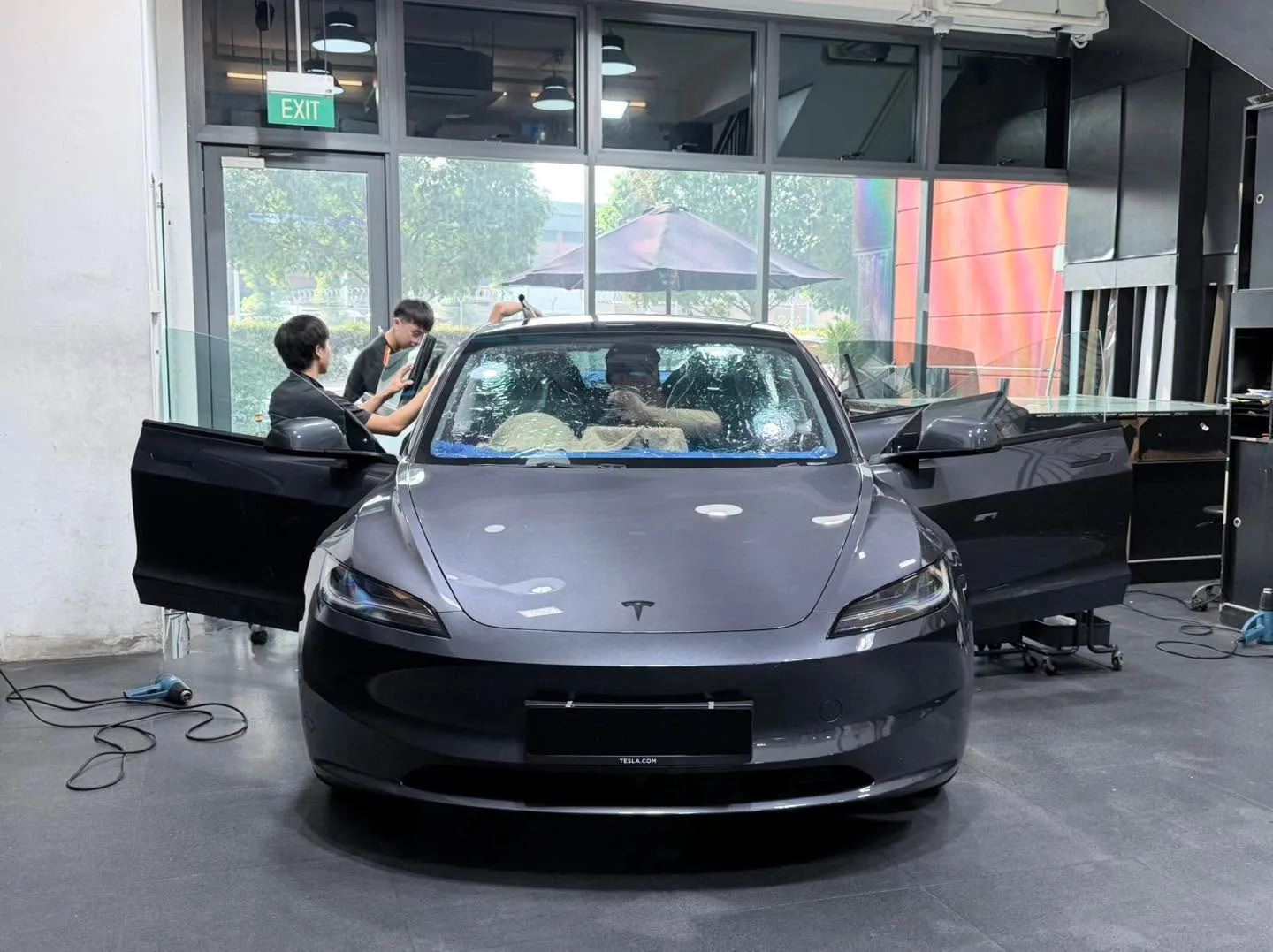 A dark Tesla sedan with both doors open as technicians work on the windows.