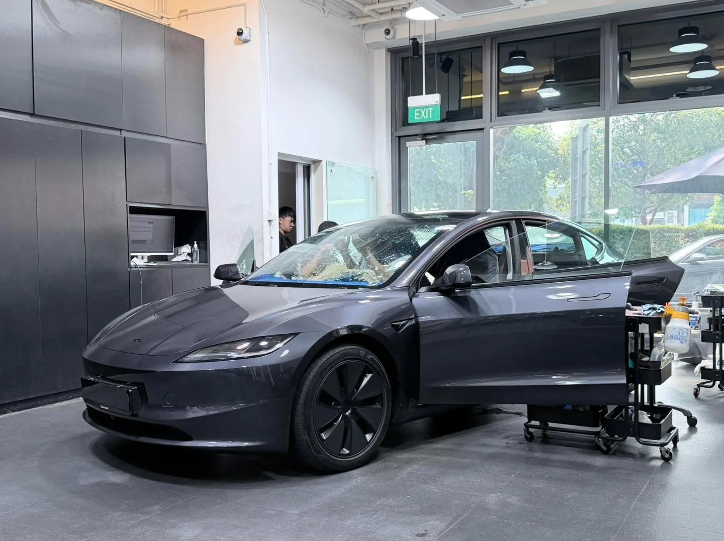 A dark Tesla sedan with the door open in the workshop.