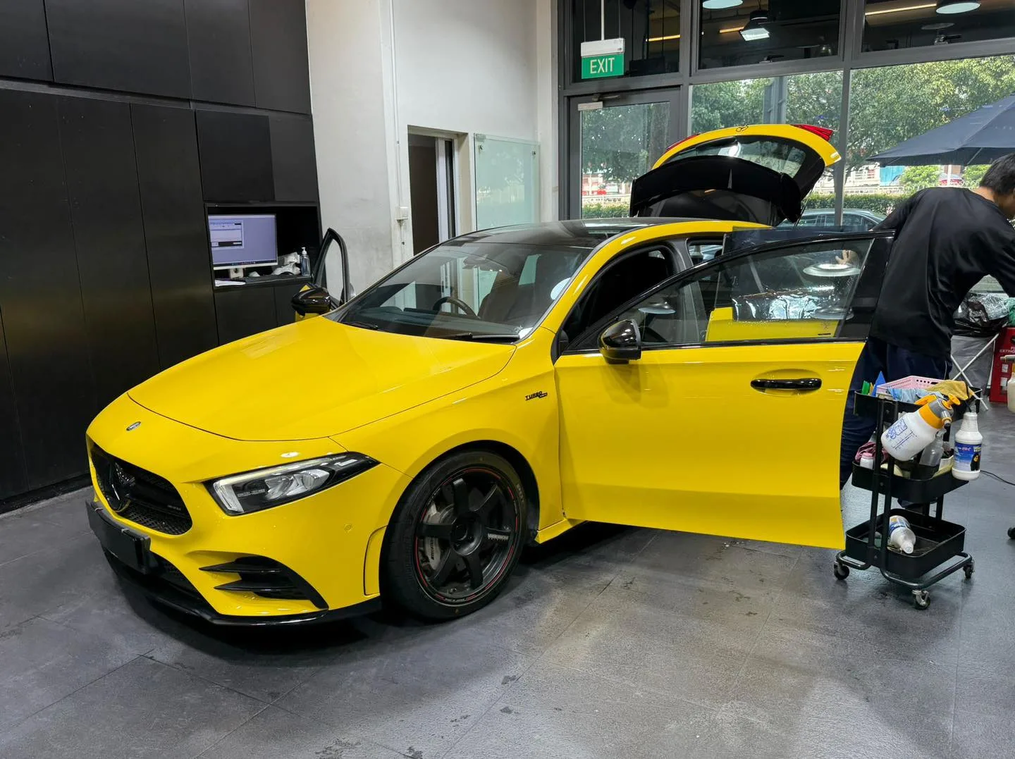 The same bright yellow Mercedes-Benz with both doors open, technician applying window film to one side.