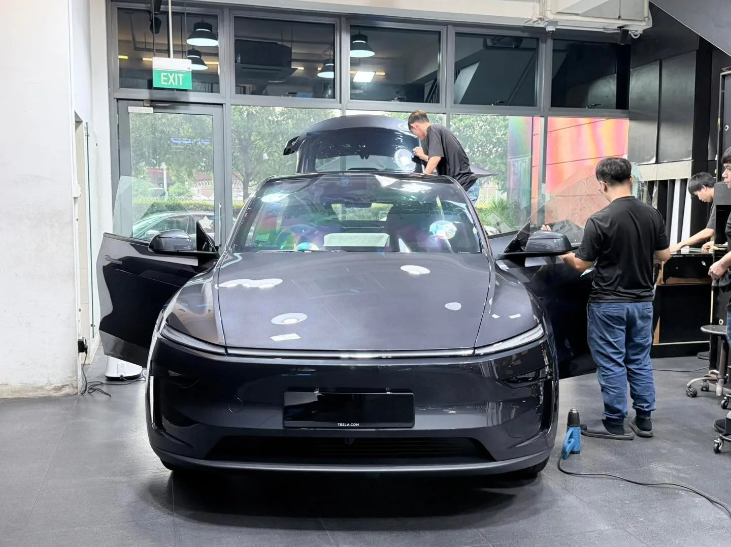 A white Mercedes-Benz sedan with both doors open, technicians applying window film inside the workshop.