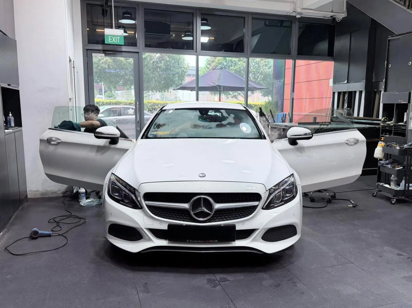 A white Mercedes-Benz sedan with doors open, technician working on the windows.