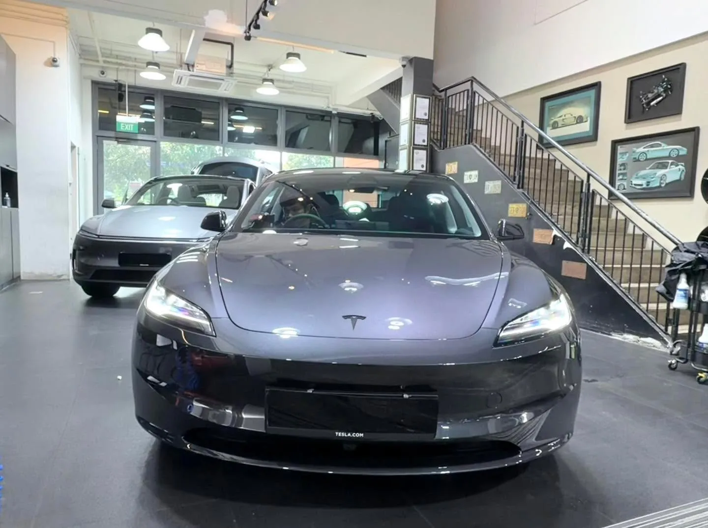 A dark grey Tesla sedan facing the camera in the workshop.