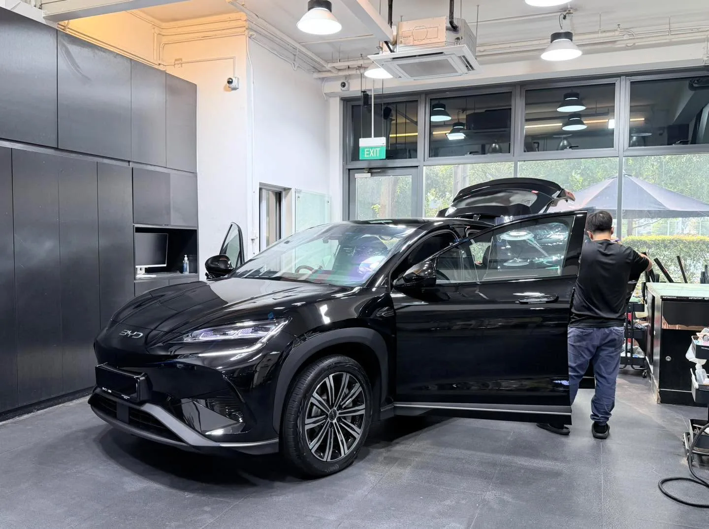 A black BYD Sealing hatchback with doors open as technicians apply film.