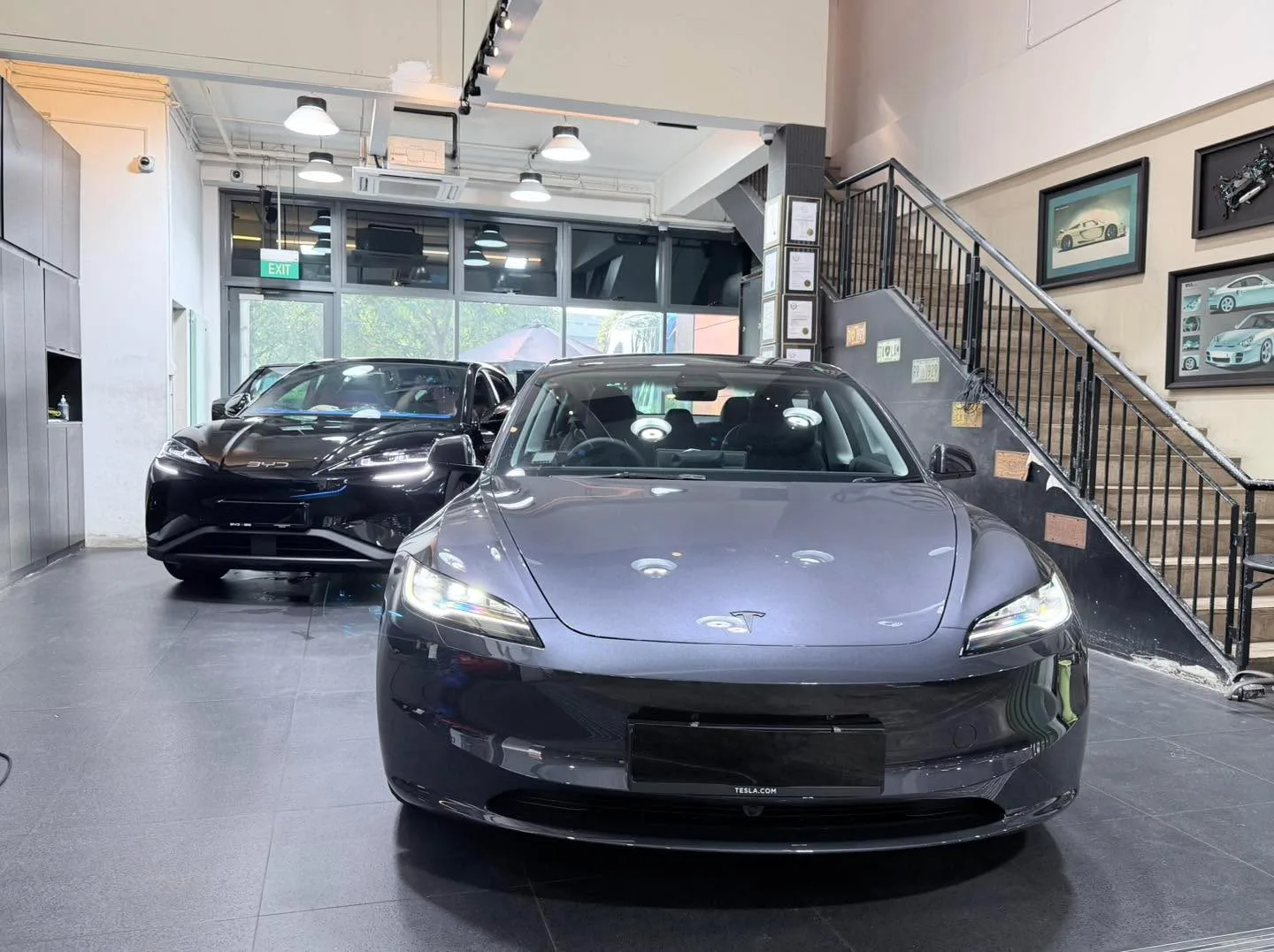 A grey Tesla sedan and a black BYD Sealing hatchback parked together in workshop.