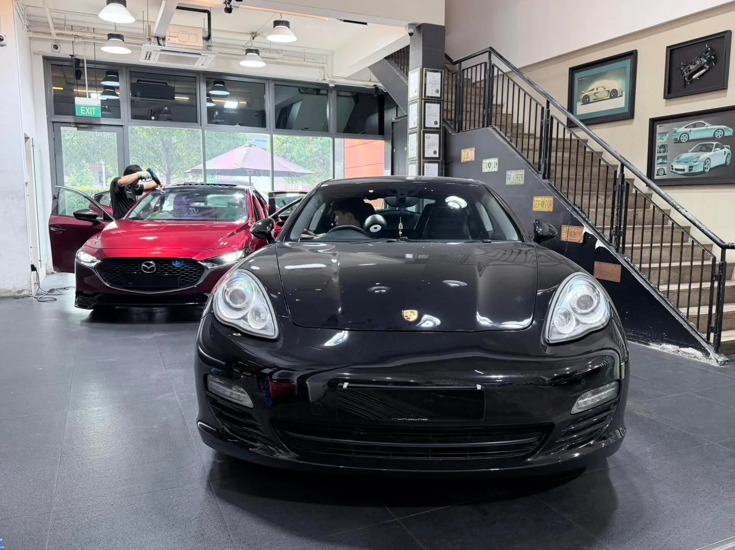Black Porsche Panamera front view in workshop with stairs and artwork visible.