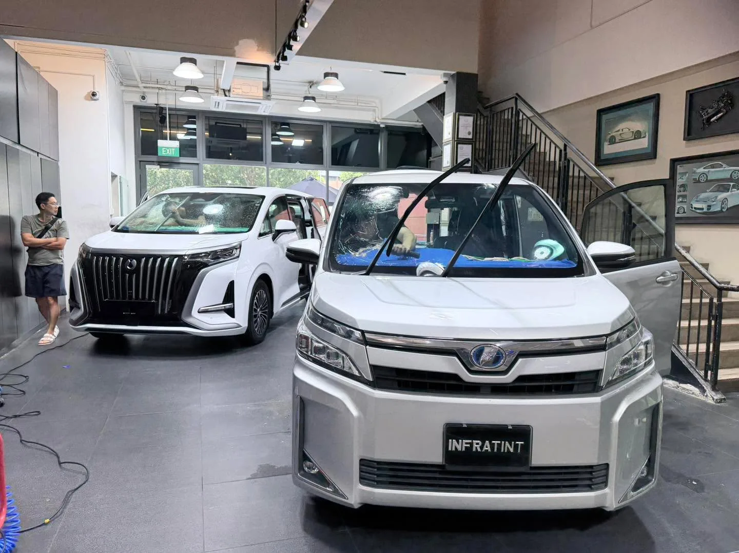 White Denza D9 SUV and white Toyota Noah MPV in workshop.