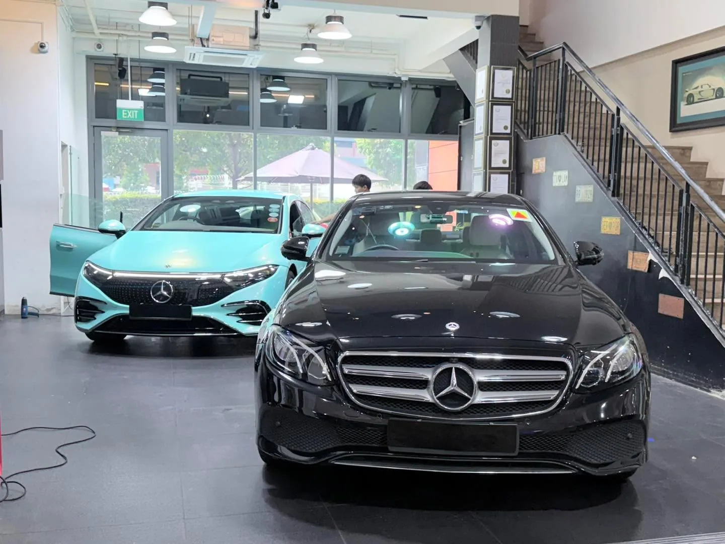 A turquoise Mercedes-Benz hatchback and a black Mercedes-Benz sedan parked side by side in the workshop.