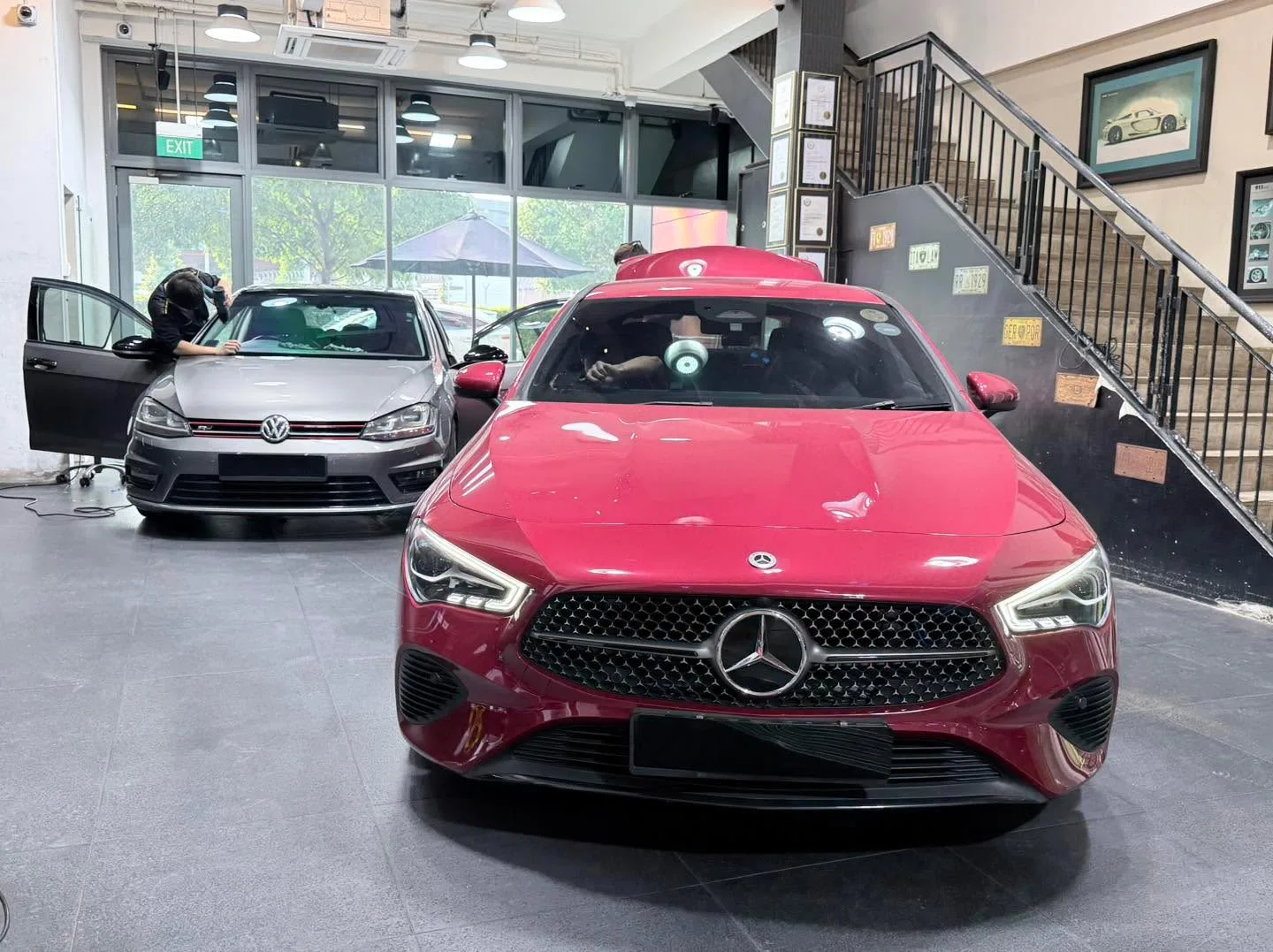 A red Mercedes-Benz compact crossover and a silver Volkswagen hatchback with its door open in the workshop.