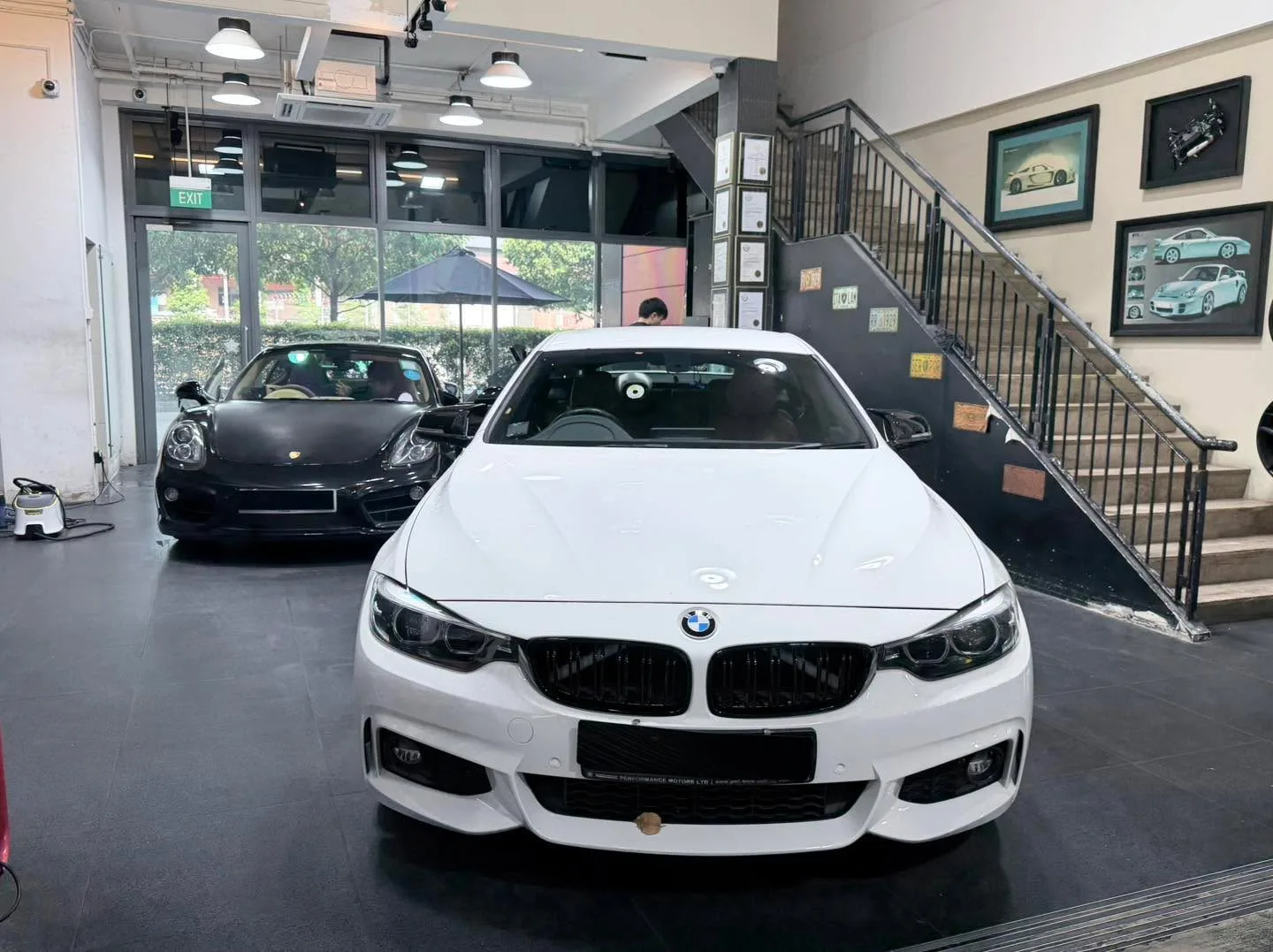 A white BMW coupe and a black Porsche sports car parked in the workshop.