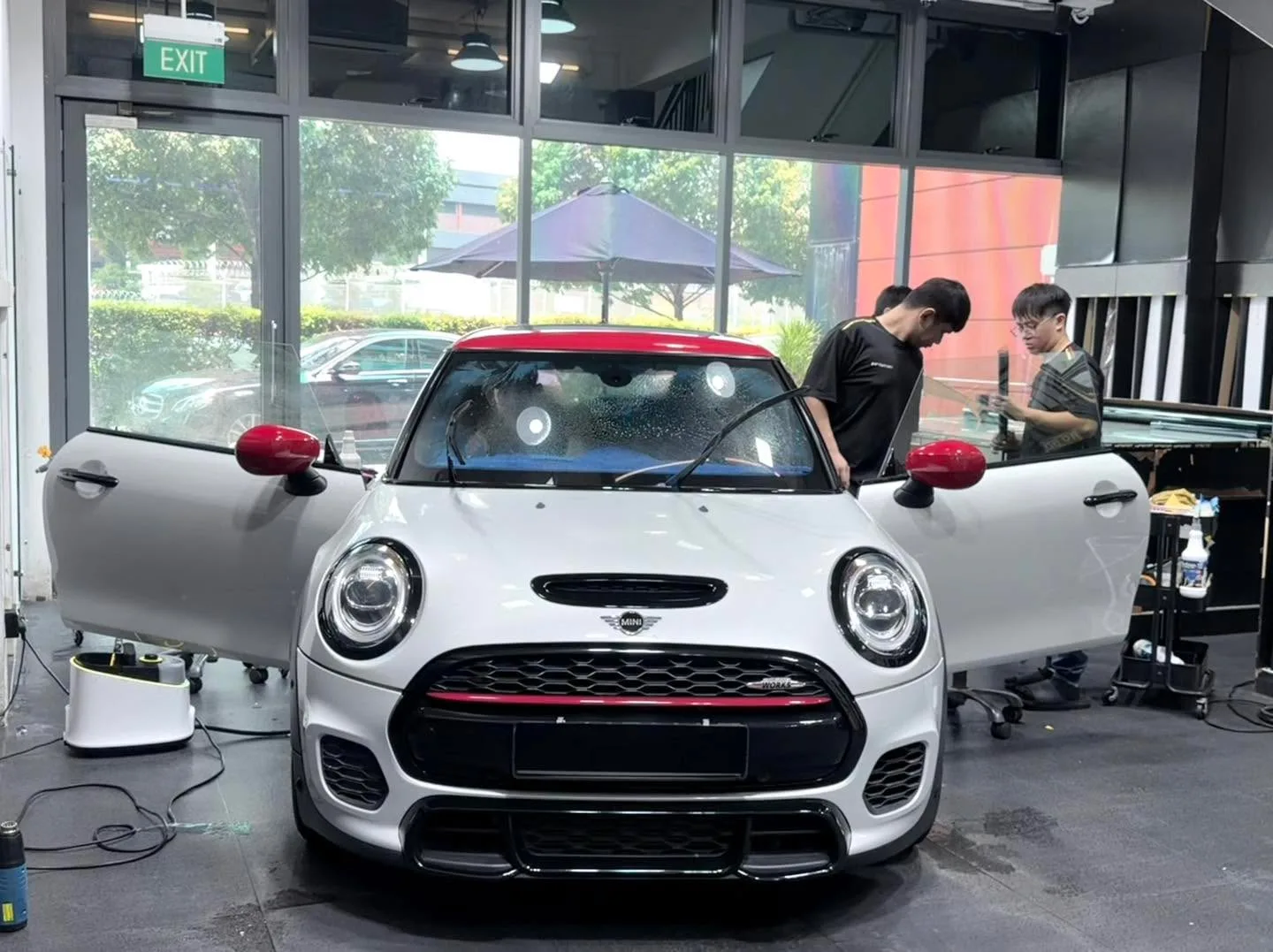 A white Mini hatchback with red mirror caps and door sill trim, both doors open, during tinting work.
