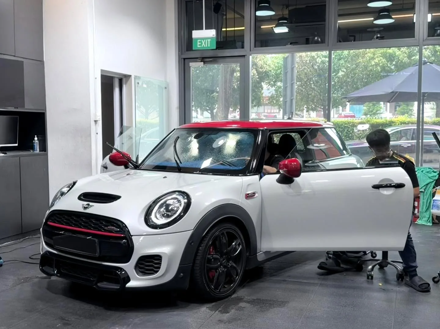 A white Mini hatchback with red accents undergoing window tinting work.