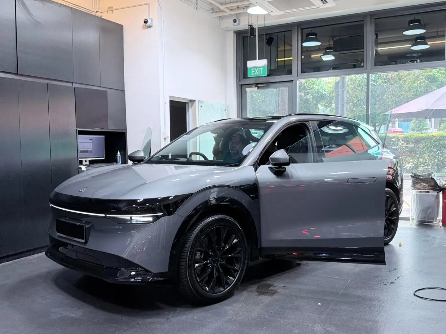 A light grey Zeekr SUV with doors open in the workshop during tinting work.