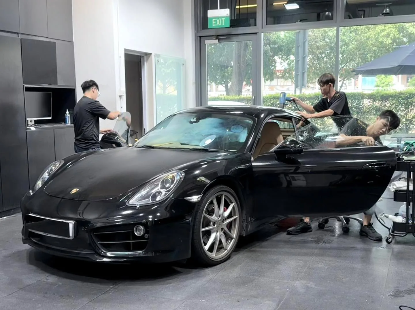 A black Porsche sports car with its door open during window tinting work.