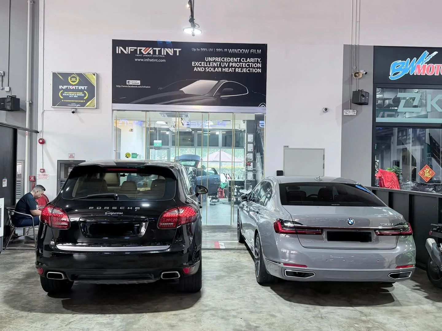 A black Porsche station wagon and a grey BMW sedan parked side by side in a workshop bay.