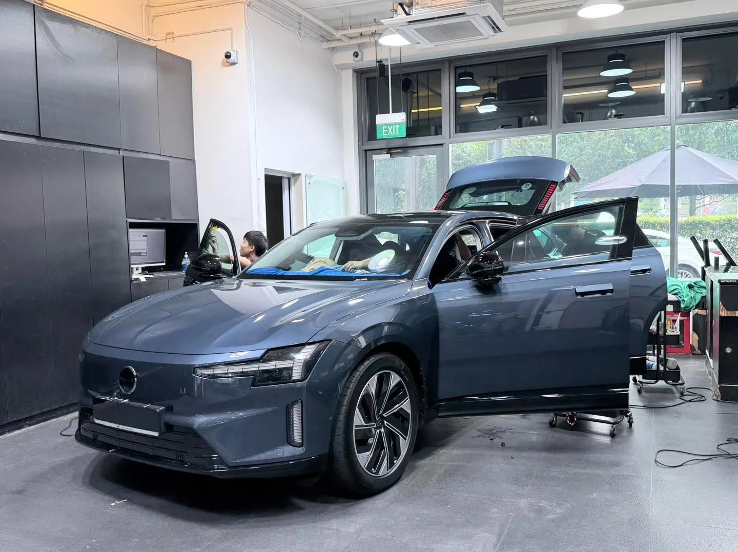 A blue BMW sedan with gull-wing doors fully open in the workshop.