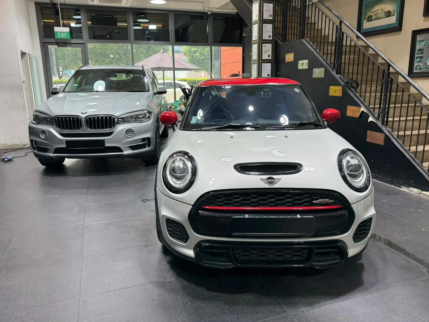 A white Mini hatchback with circular headlights and a white BMW X5 SUV parked indoors.