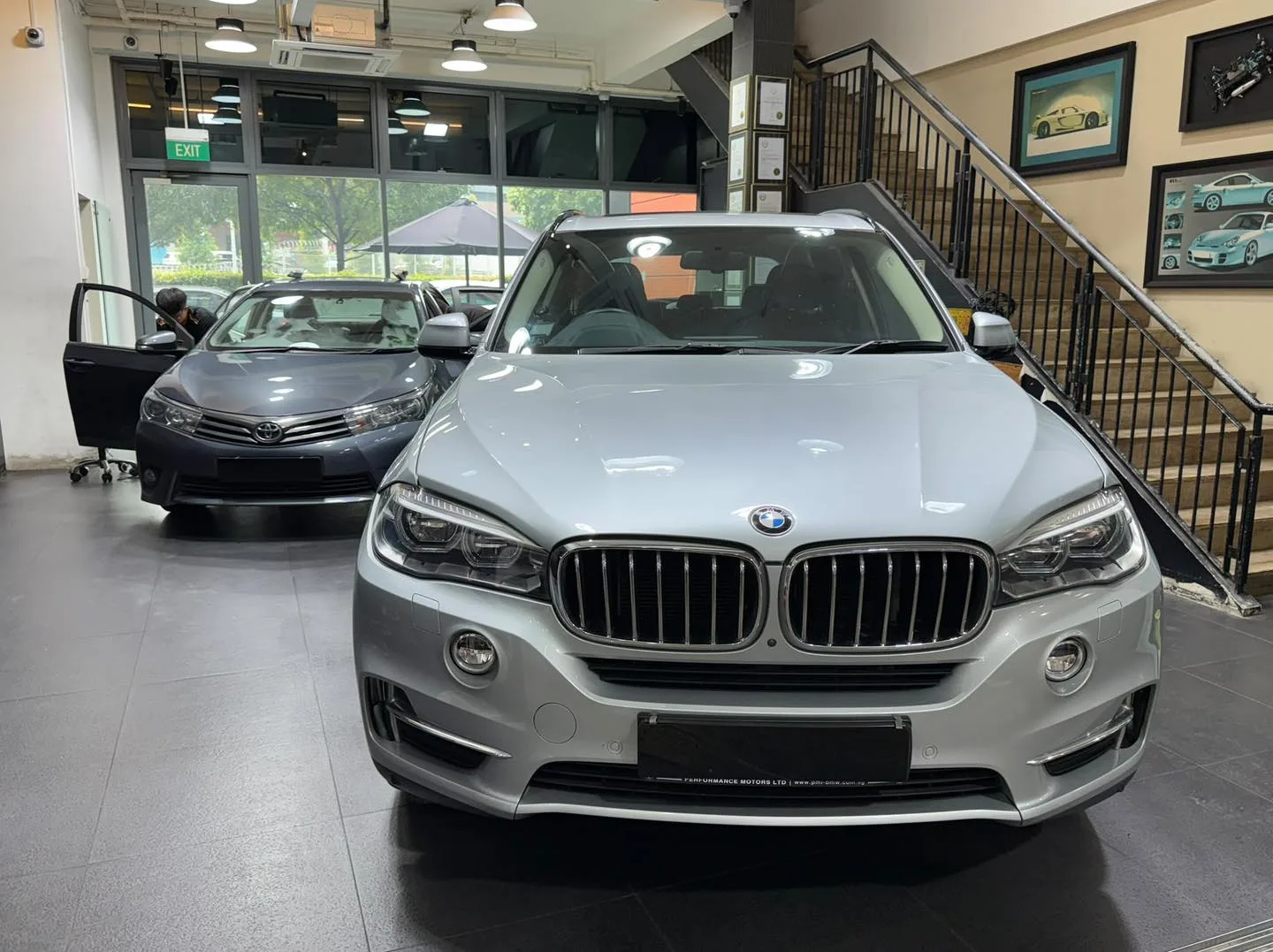 A silver BMW X5 SUV and a white BMW sedan seen from the front indoors.