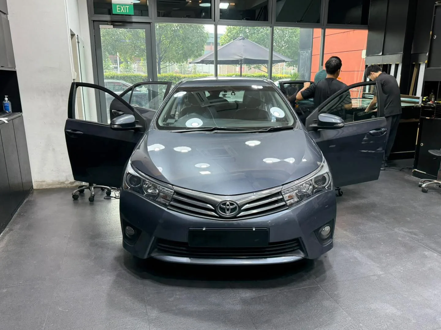A dark grey Toyota Altis saloon with doors open, undergoing tinting.