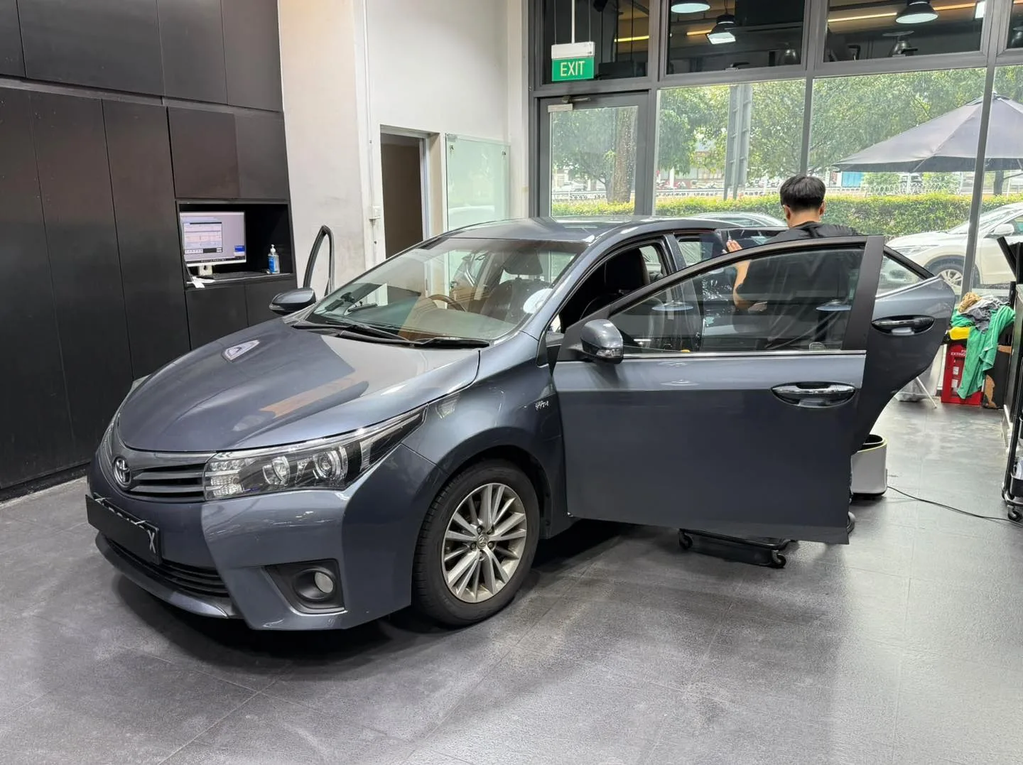 A dark grey Toyota Altis saloon with doors open indoors.
