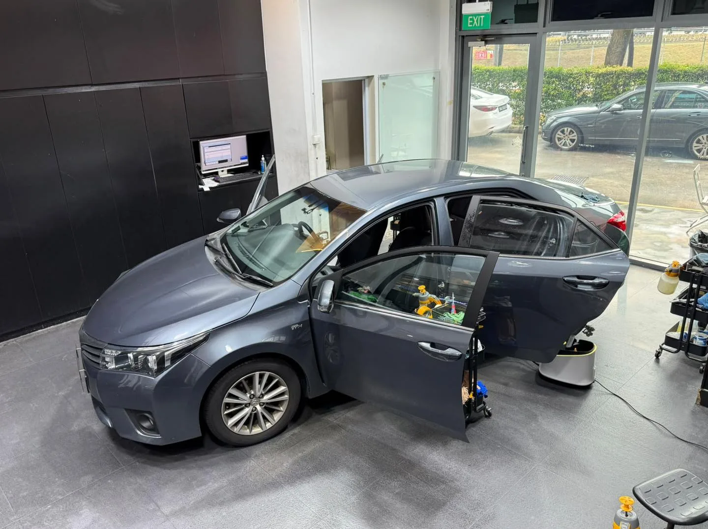 A dark grey Toyota Altis with driver door open for tinting work.
