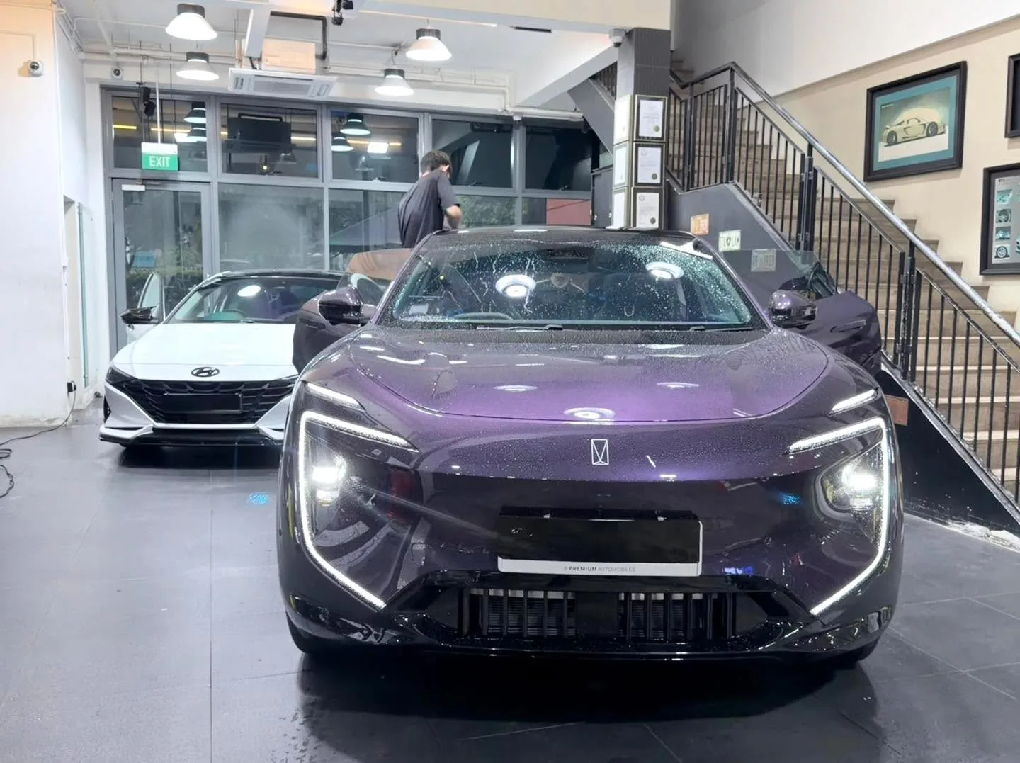 A purple sedan with distinctive headlights, seen from the front, parked indoors next to a white sedan.