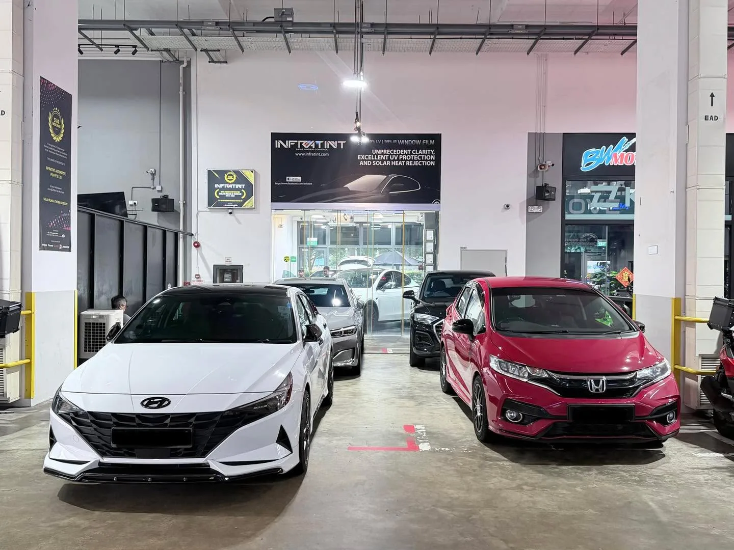 A white Hyundai sedan and a red Honda hatchback parked in the workshop bay.