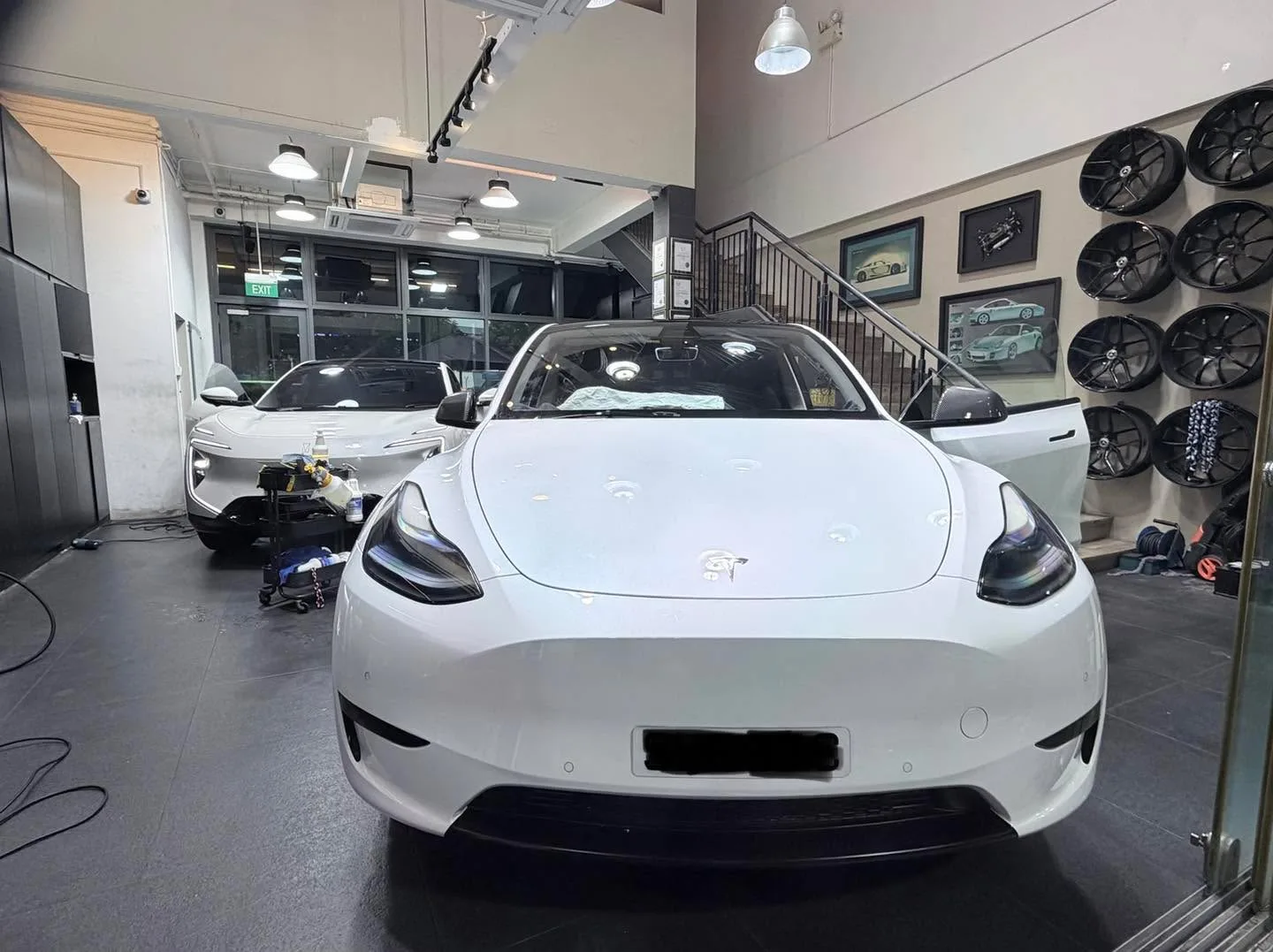 A white Tesla sedan parked in an indoor workshop with equipment visible.