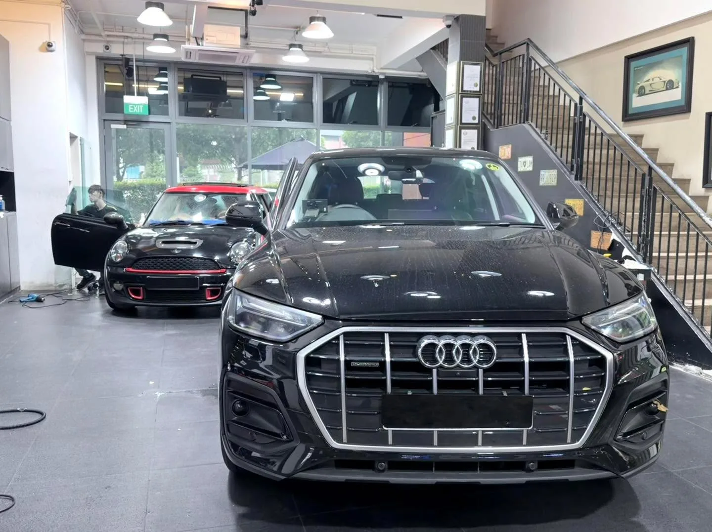 A black Audi Q5 SUV parked indoors next to a black Mini compact car.