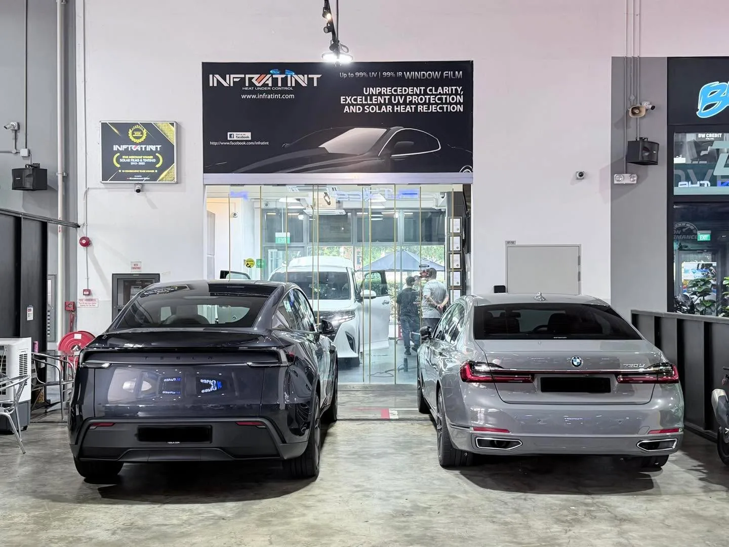 A black Tesla Model Y and a silver BMW 7 Series parked in the workshop.