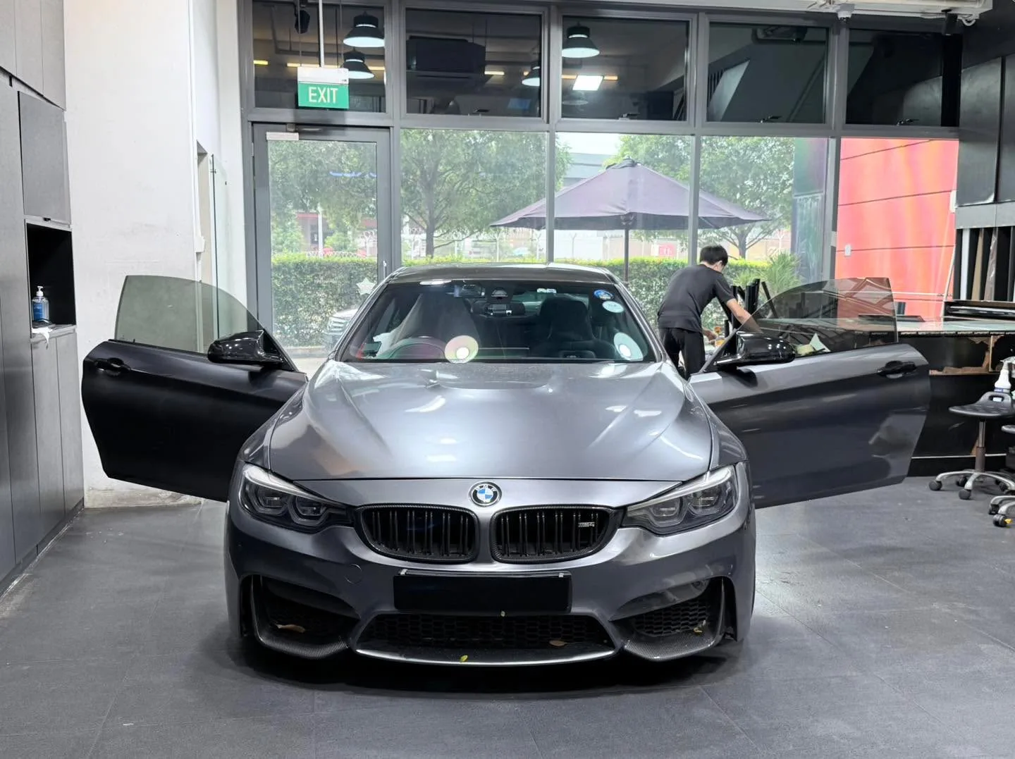 A grey BMW M4 with doors open inside the workshop.
