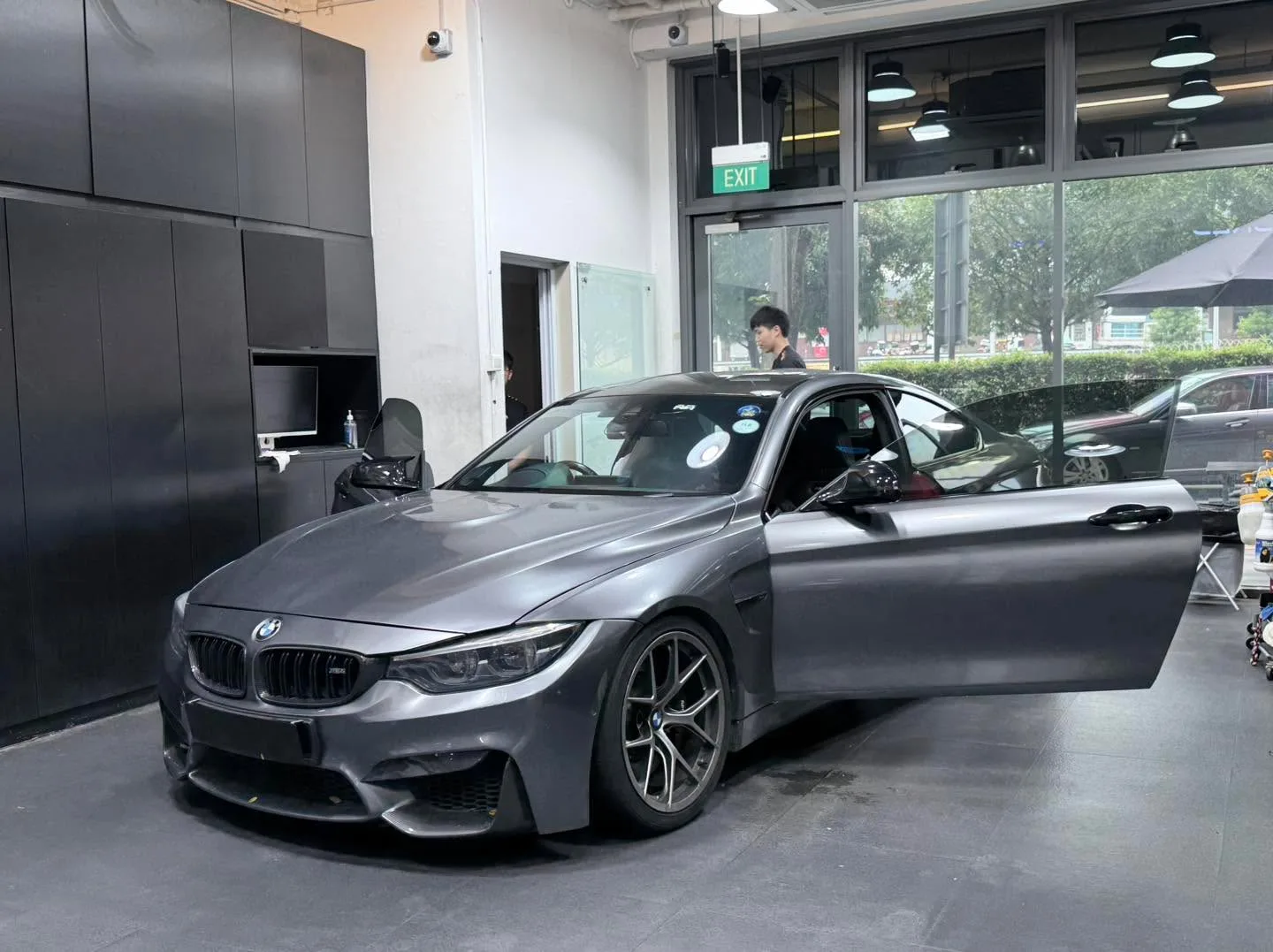 A grey BMW M4 coupe with the door open in the workshop.