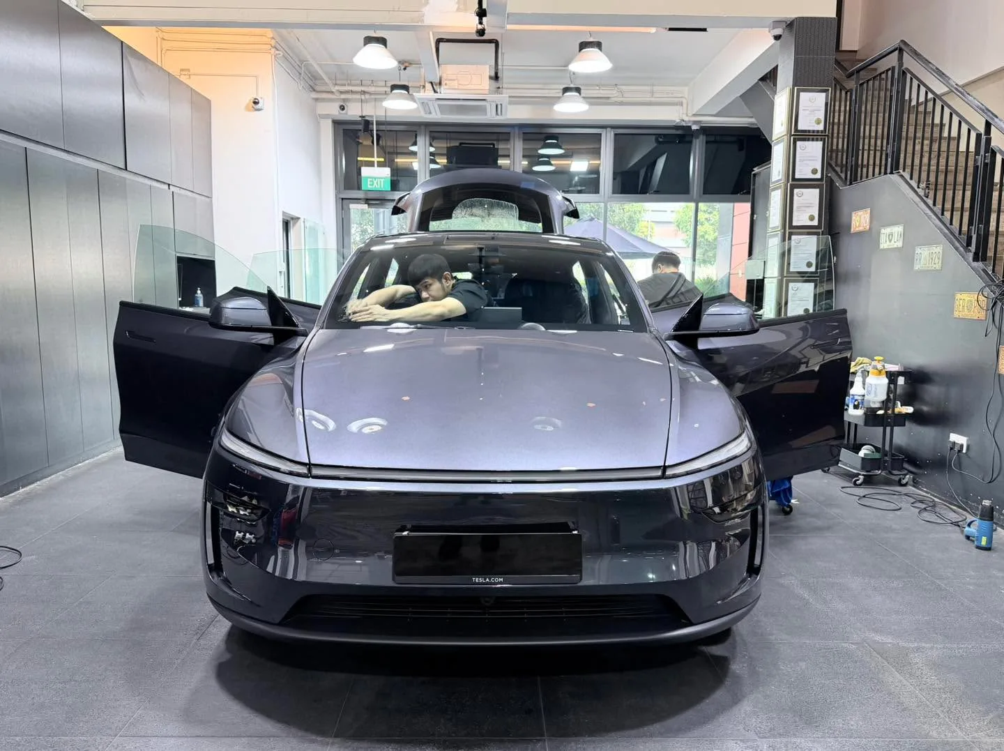 A dark grey Tesla Model Y with doors open inside the workshop.